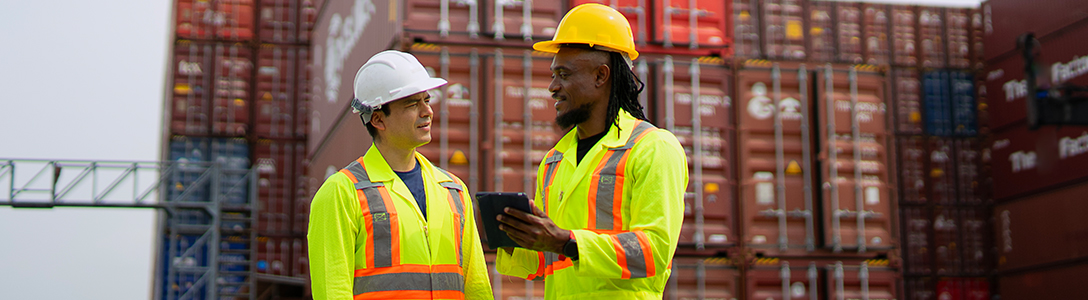 Industrial supply chain professionals using a tablet to review logistics data at a shipping container terminal. Industrial supply chain professionals using a tablet to review logistics data at a shipping container terminal.